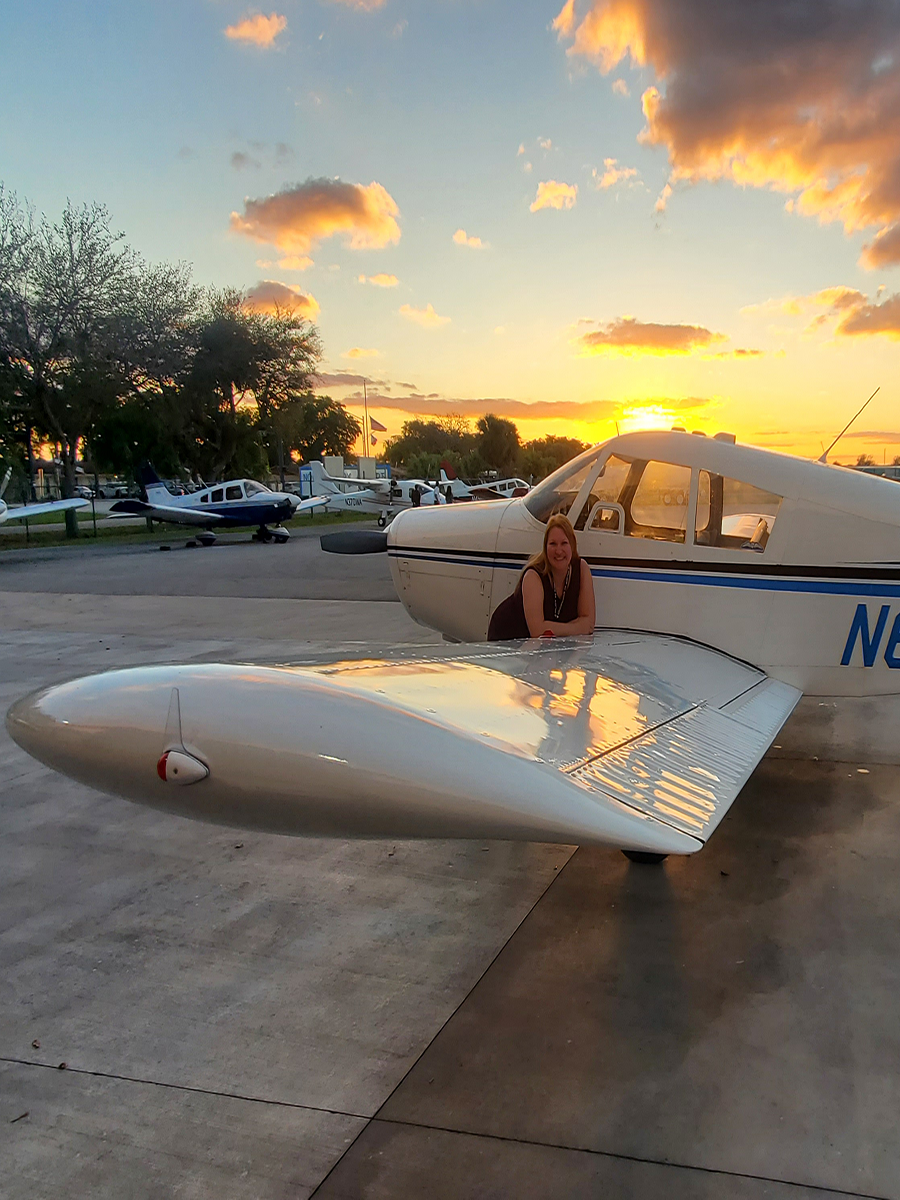 an image of katie during a sunset leaning on the wing of her piper